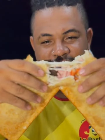 Homem com a camiseta da Le Pastéis mordendo um pastel aberto