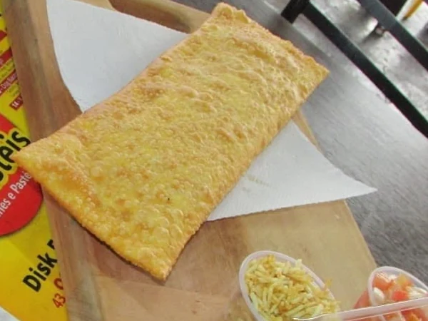 Pastelão dourado sobre uma tábua de madeira, com potinhos de batata palha e vinagrete ao lado